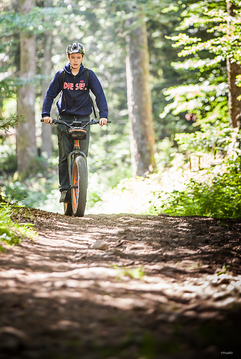 Jeune personne pratiquant le VTT sur un sentier forestier en montagne.