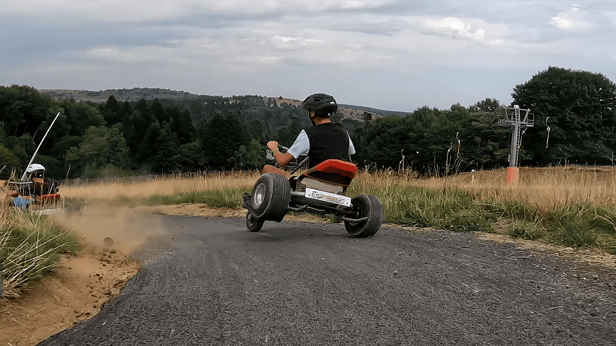 Une personne en kart tout-terrain dévale un chemin goudronné en pleine montagne, soulevant de la poussière dans un virage.