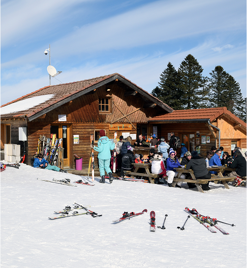 Chalet en bois à Prabouré avec guichet de forfaits de ski et skieurs se reposant à l’extérieur.