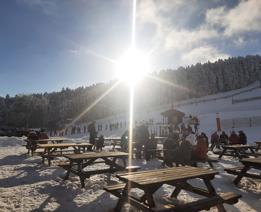 Terrasse enneigée de la station de Prabouré avec skieurs et visiteurs profitant du soleil.